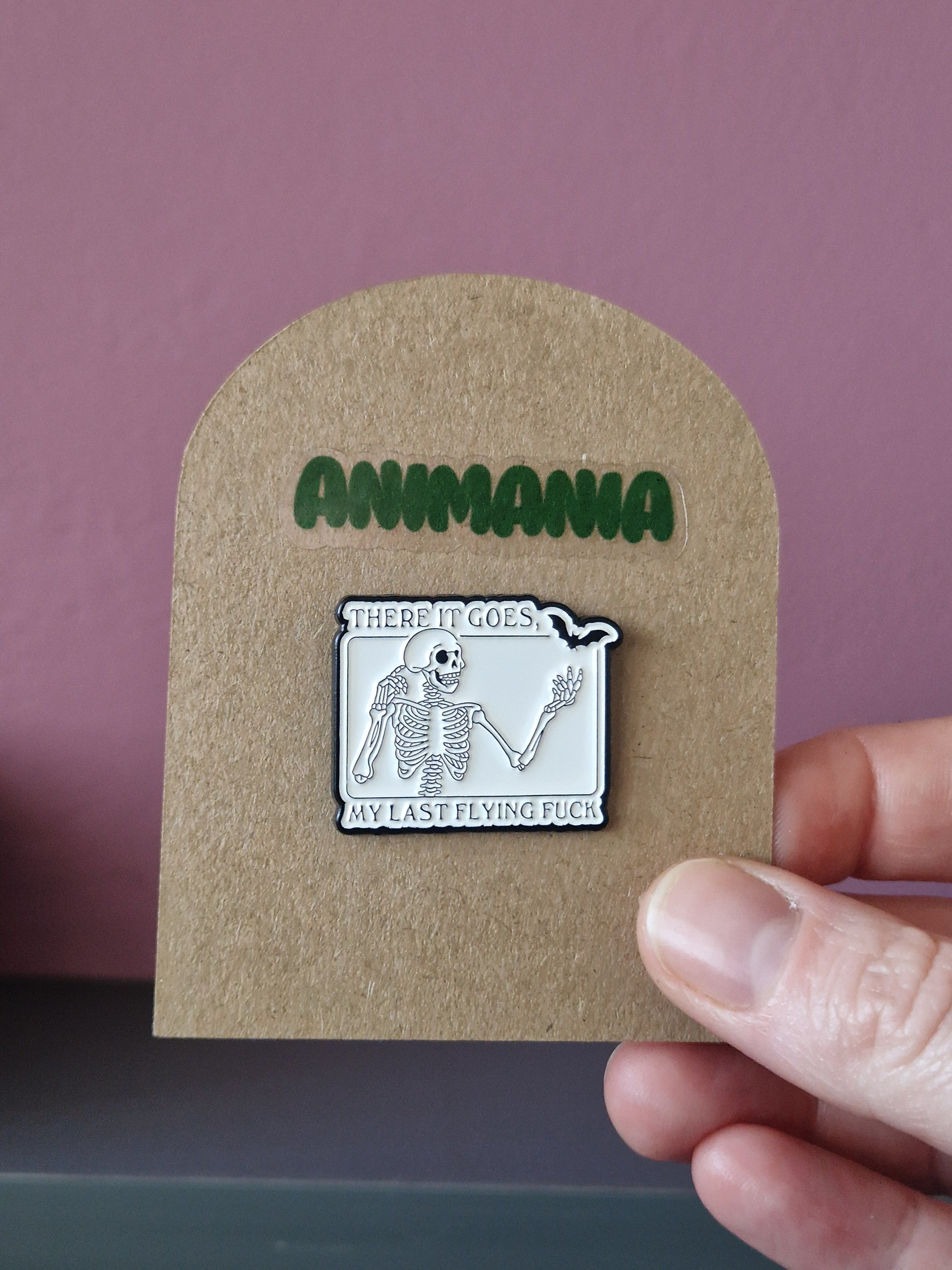 A black and white skeleton & bat pin with 'there it goes, my last flying fuck' written above & underneath it. Pin is mounted on a brown cardboard backing with the brand Animania written above it.