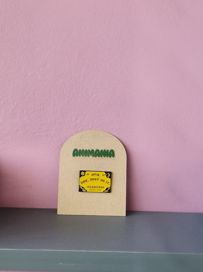Yellow Ouija board pin that says 'How don't do it' centrally. Pin is mounted on a brown cardboard backing with the brand Animania written above it.
