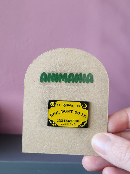 Yellow Ouija board pin that says 'How don't do it' centrally. Pin is mounted on a brown cardboard backing with the brand Animania written above it.