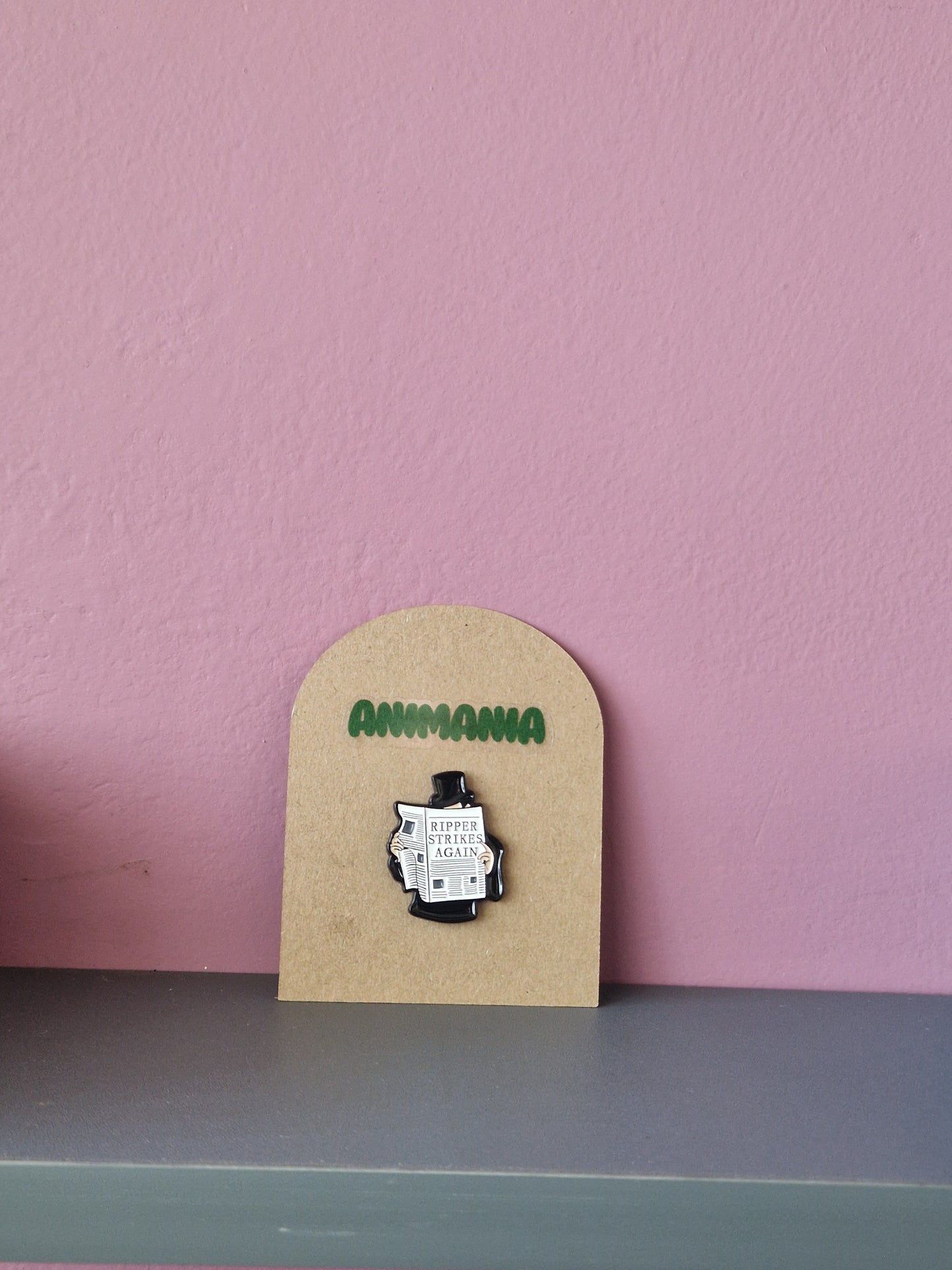 Jack the ripper pin that says 'ripper strikes again' on a newspaper. Pin is mounted on a brown cardboard backing with the brand Animania written above it.